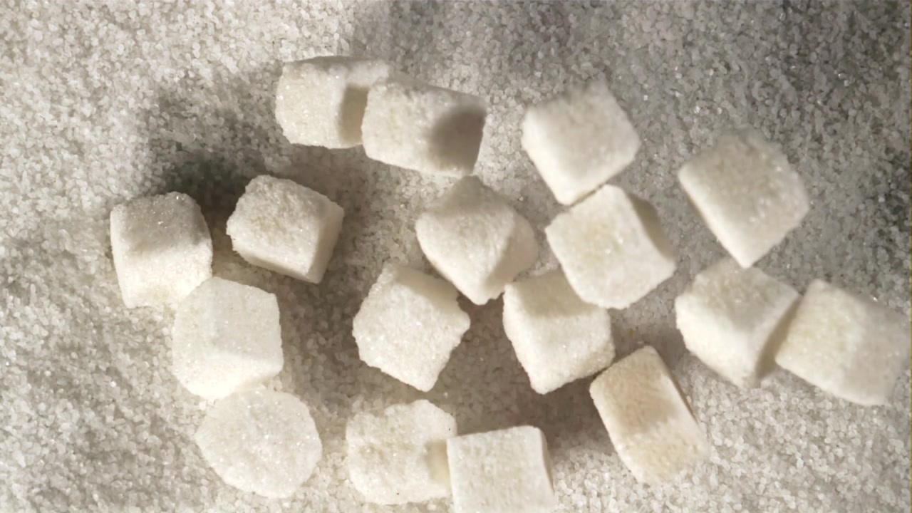 Cámara lenta de terrones de azúcar cayendo sobre azúcar granulada