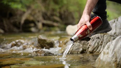 hand empties bottle into stream of water in natural landscape