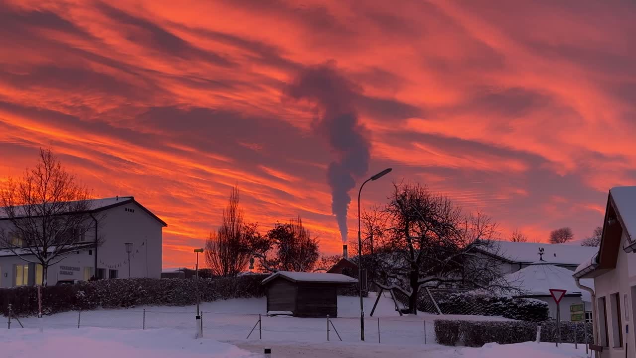 Scena invernale mattutina poco prima dell'alba con spettacolari nuvole arancioni e fumo che si alza da una centrale elettrica a Lembach im Mühlkreis, in Austria. Tranquillo paesaggio di paese con neve e atmosfera industriale