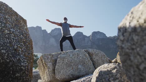 senior african american man exercising stretching on rocks by the sea