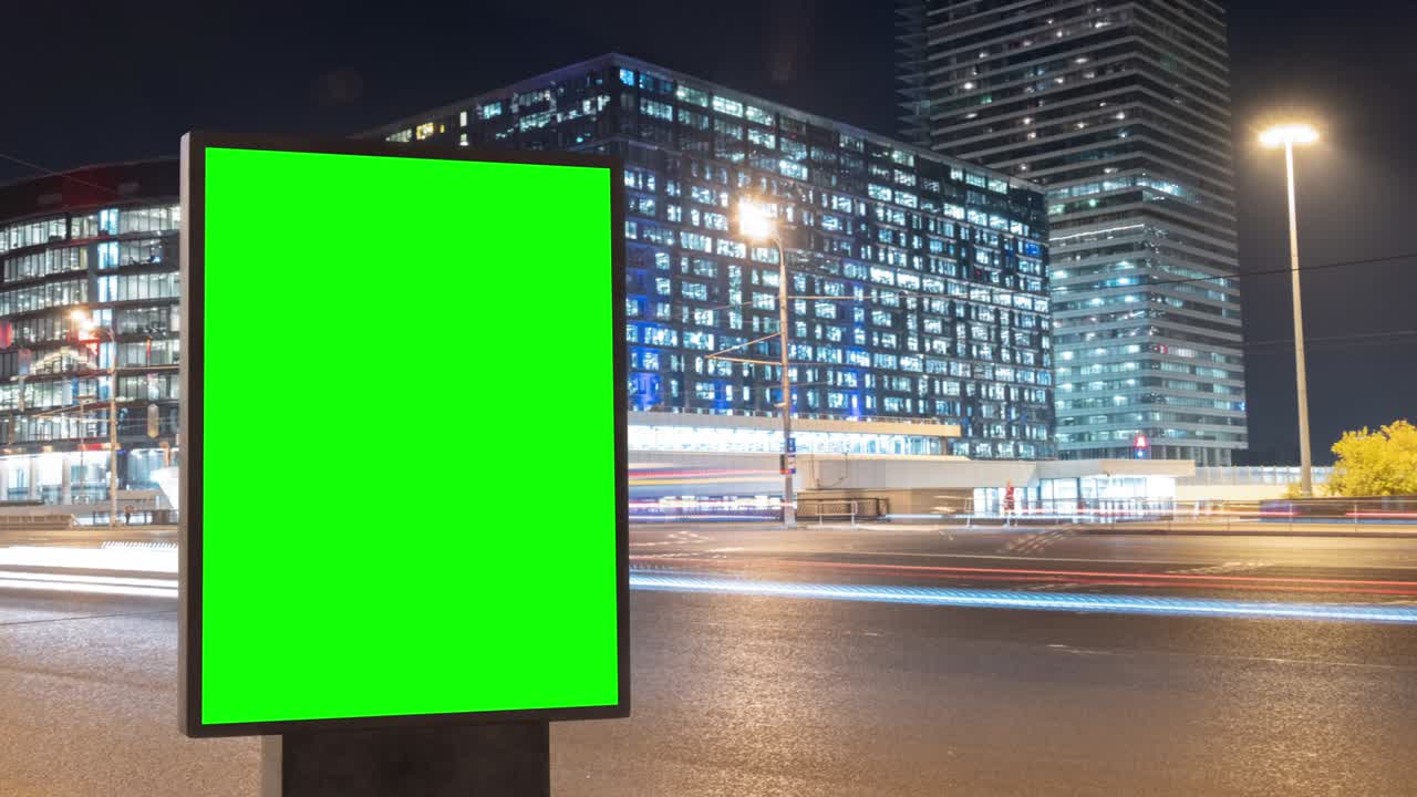 Modern billboard with a green screen for advertising on a busy highway with traffic and skyscrapers, timelapse of traffic at night