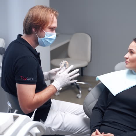 pretty woman talking to a stomatololist. male dentist showing artificial jaw to a patient at the dental office. dental concept.