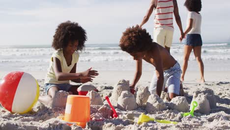 hermano y hermana afroamericanos jugando con arena en la playa