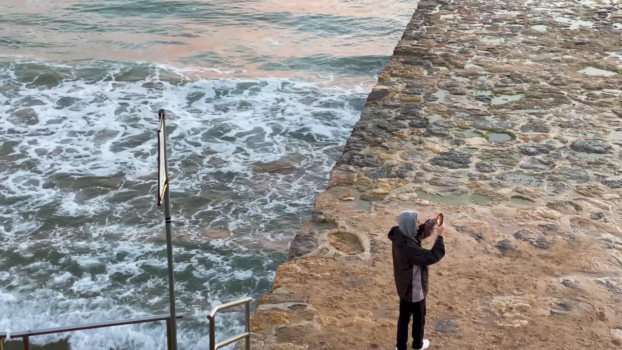 모자와 옷을 입은 남성 여행자가 놀라운 일몰의 파노라마 사진을 찍습니다.