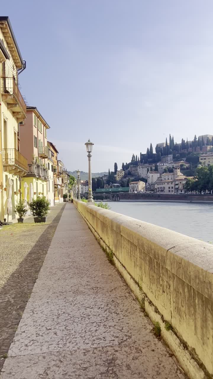 Wonderful Italian landscape walkway with colourful houses, River Adige and Castel San Pietro in the background on a clear sunny summer morning