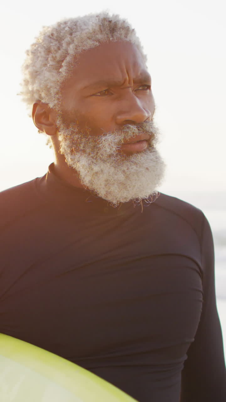 Happy senior african american man walking with surfboard on sunny beach