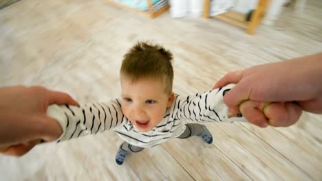 little boy spinning around and around laughing and smiling at the end of his fathers arms at home