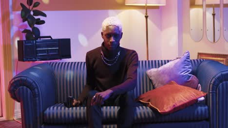 african american man with blonde hair taking pictures to the camera while sitting on sofa in a retro room at home