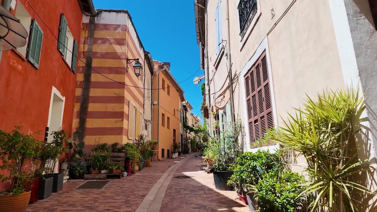 Una carrellata dal basso si muove attraverso un vivace e stretto vicolo mediterraneo sotto la luce intensa del sole.