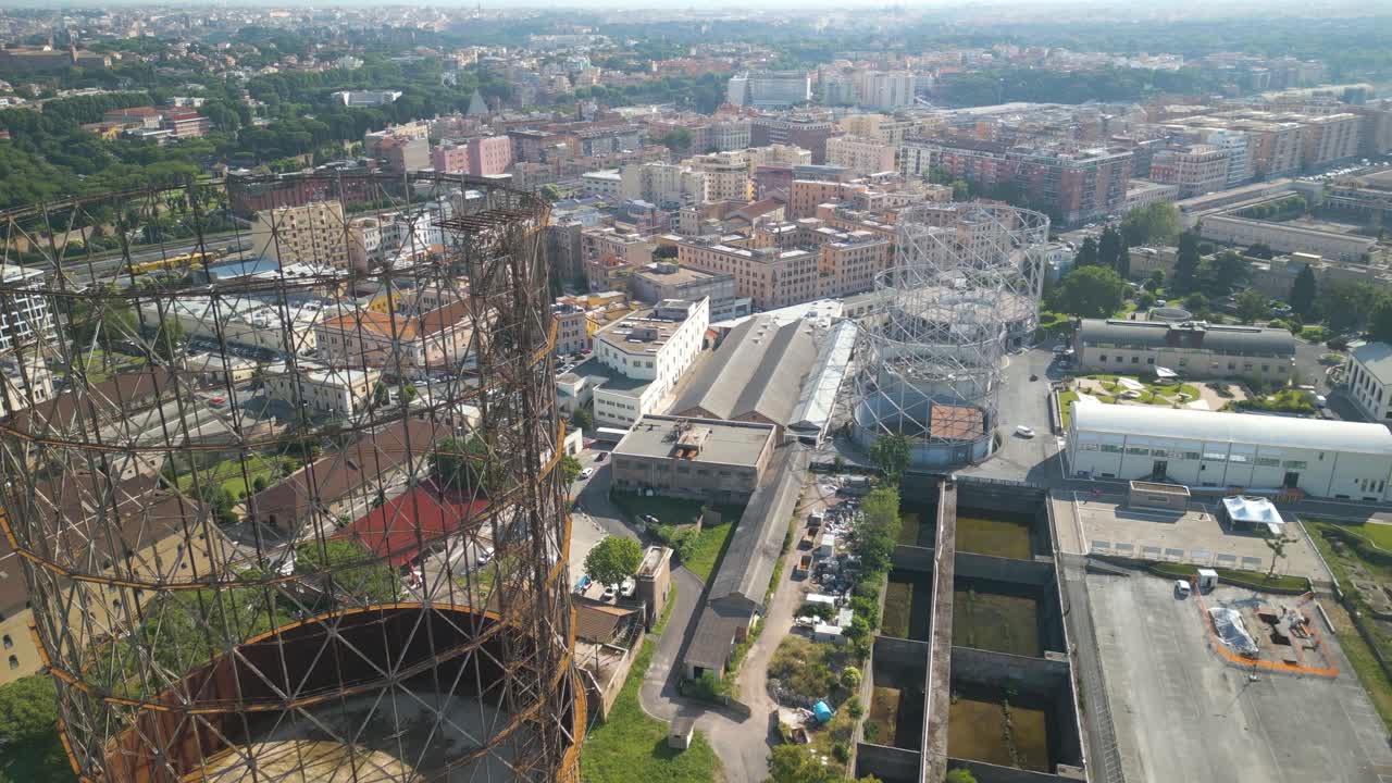 avión no tripulado hacia adelante disparo en movimiento volando alto sobre la vieja estructura de hierro, gazómetro con la vista del distrito de ostiense, roma en italia en un día soleado
