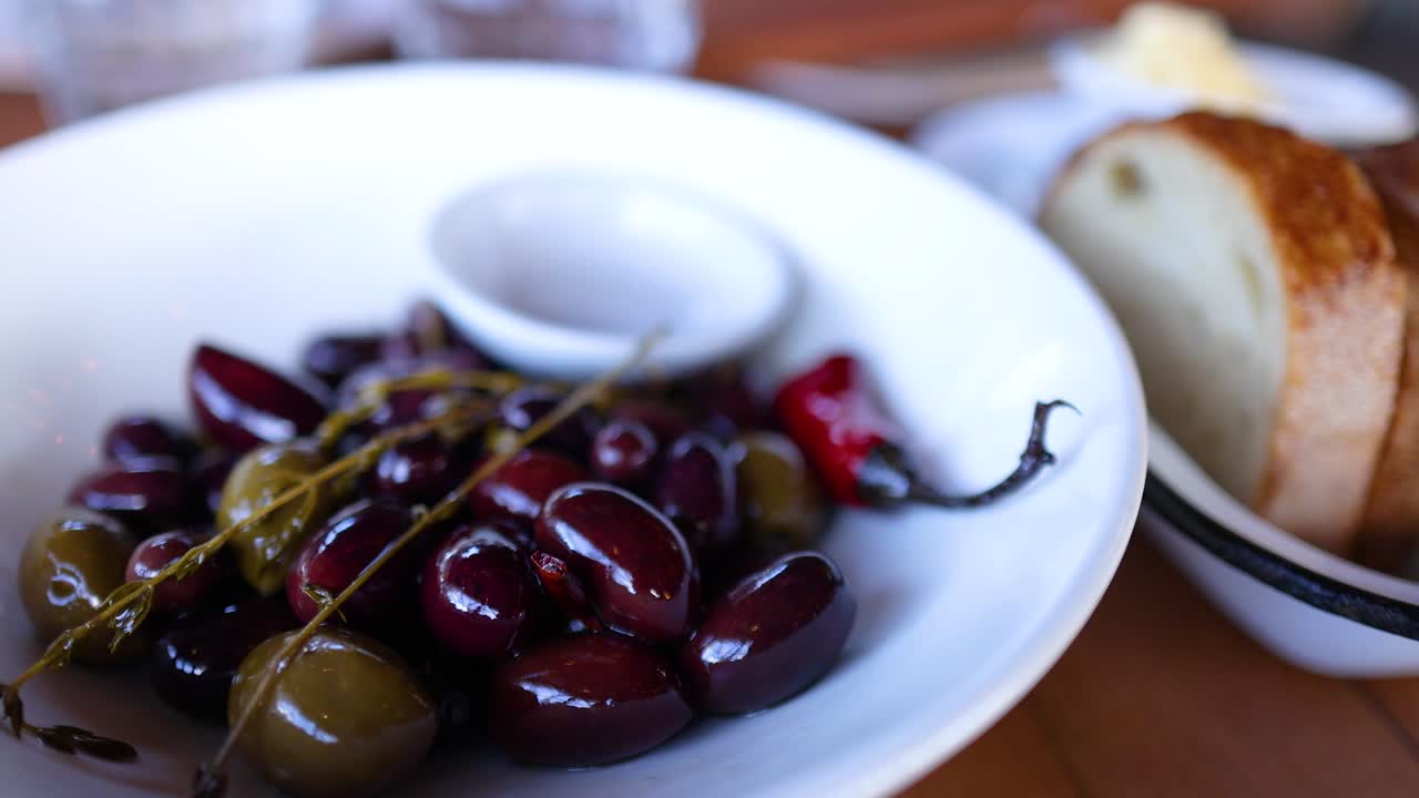 A close-up of herb roasted olives and sliced bread on a wooden table, captured in natural lighting