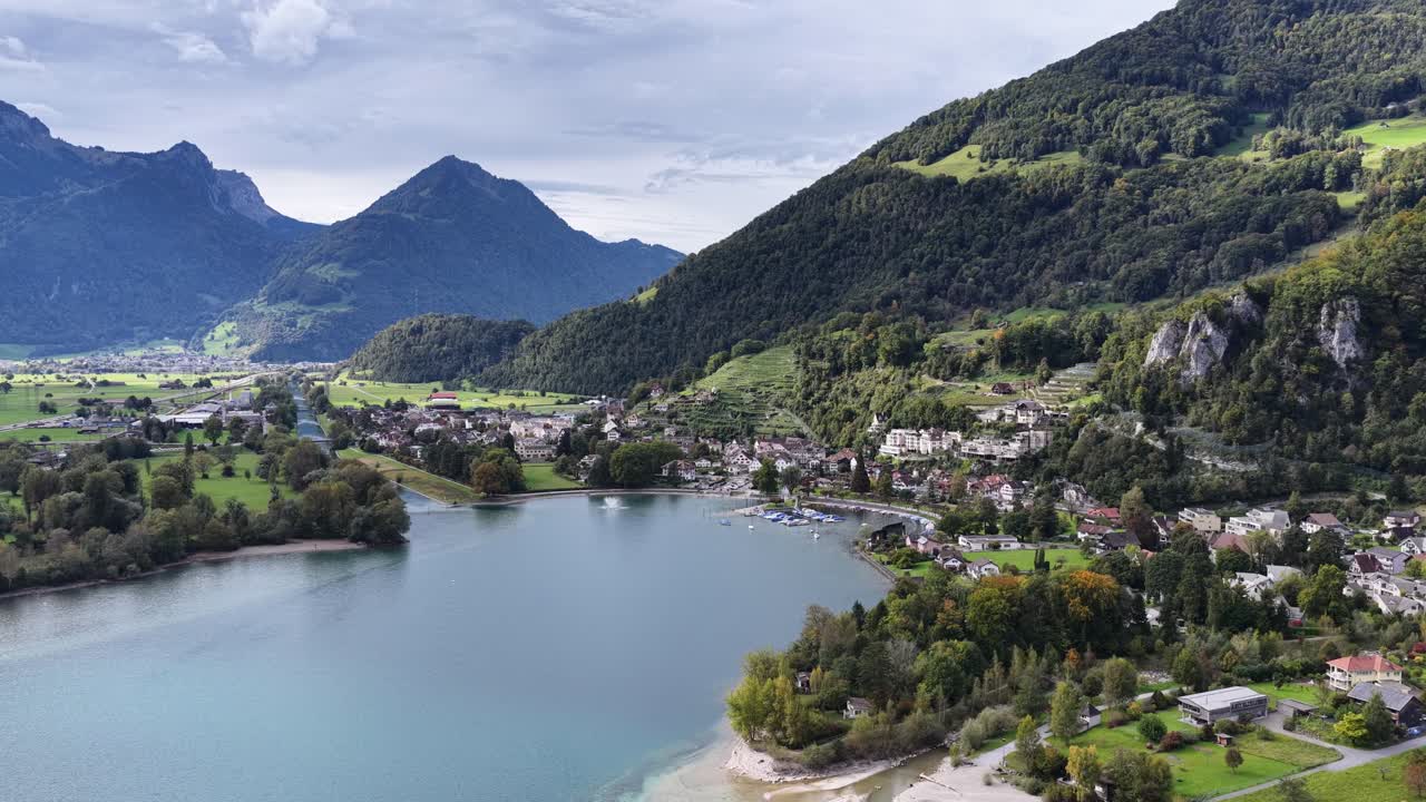 The Walenstadt harbor and town sit against the steep, forested slopes rising from the Walensee under a moody sky in Schweiz. Concept: Sheltered community beneath the Alpine expanse