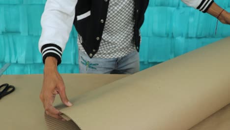 person folds corrugated cardboard on table with teal background for diy craft project