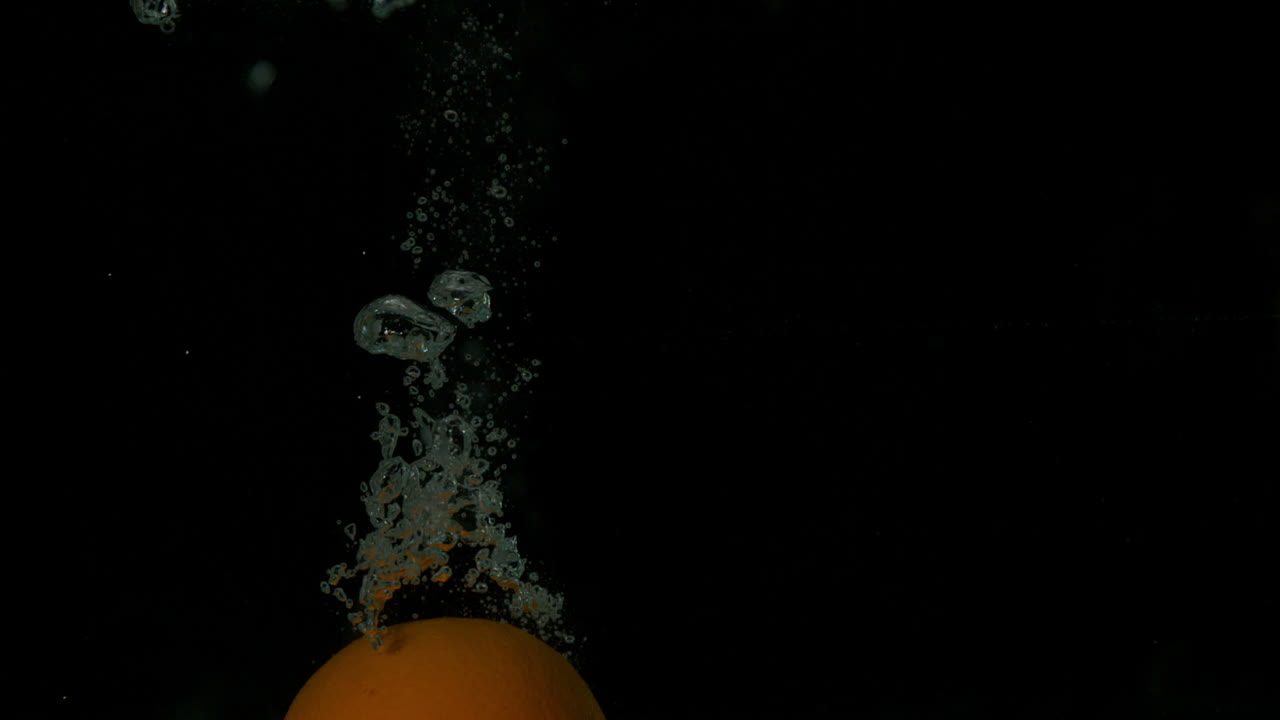 naranja sumergiéndose en el agua sobre un fondo negro
