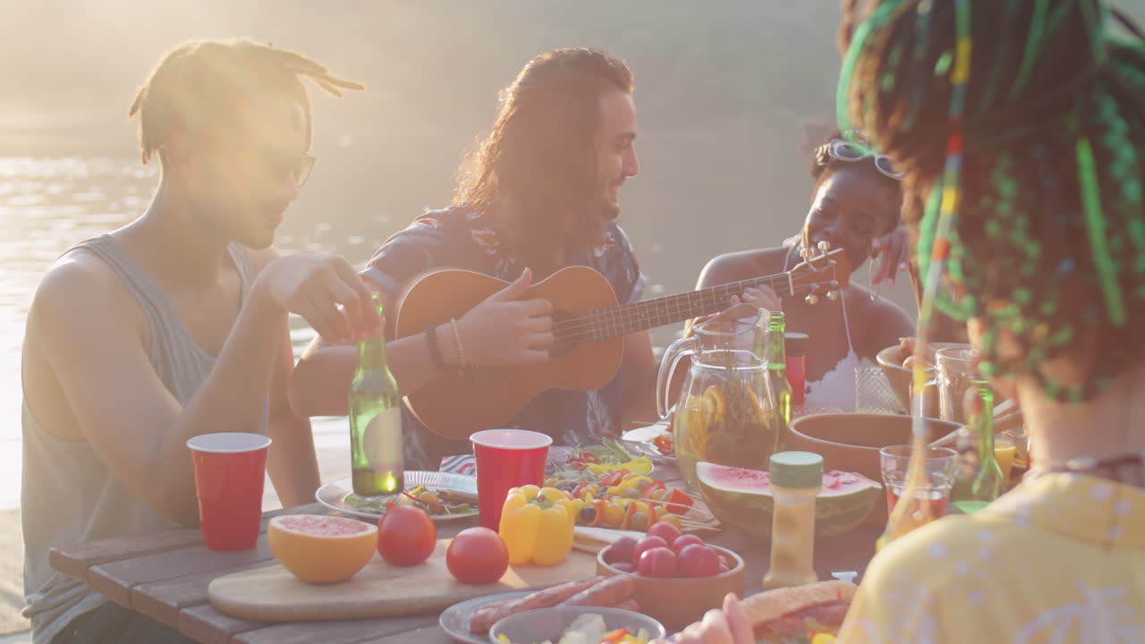 amigos felices tocando el ukulele y cantando en la fiesta del lago