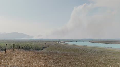 established-of-Pukaki-Downs-New-Zealand-during-big-fire-in-winter-season-2023-established-with-car-driving-on-road-and-smoke-at-distance,-tourist-evacuation