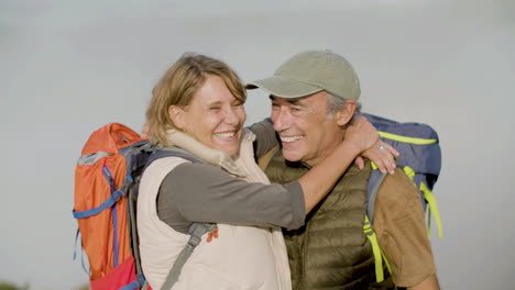 vista frontal de un excursionista senior feliz con mochilas abrazándose y besándose, luego mirando la cámara