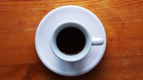 zoom down shot on a hot espress cup standing on a white plate and brown wooden table