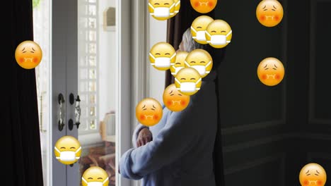 Animation-Von-Emojis-Mit-Gesichtsmasken-über-Einer-Besorgten-älteren-Frau-Am-Fenster