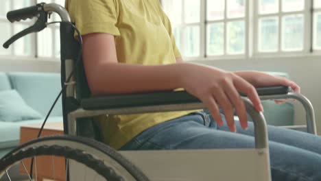 close up of asian kid girl sitting in a wheelchair smiling and showing thumbs up in living room