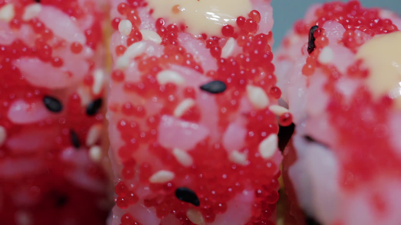 Close up of vibrant red sushi rolls topped with creamy sauce and sesame seeds, served on a ceramic plate