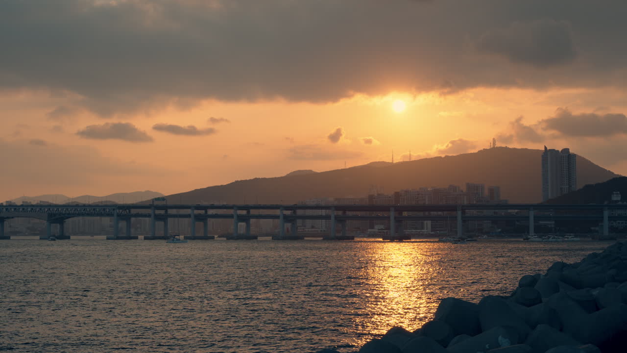 황금빛 해가 지는 황금빛의 해가 <hwangnyeongsan beacon mountain>과 <gwangan bridge>을 가로질러 바물에 반사되는 태양빛을 담고 있다.