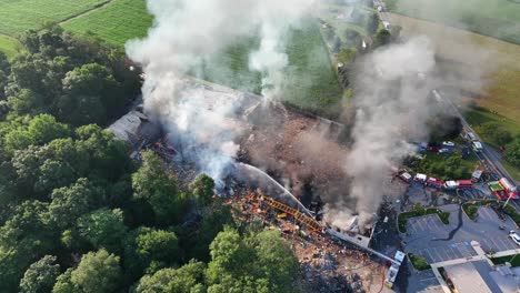 emergency response vehicles lined up on country road, smoke rising from extinguished gas explosion fire, usa