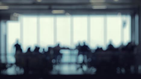 a defocused shot of many silhouettes of people walking around in a food court office building