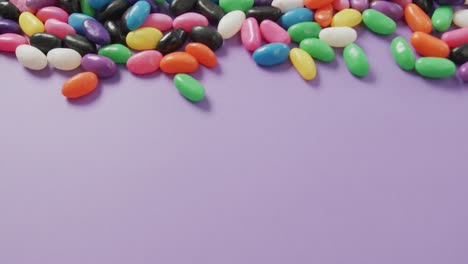 video of close up of multi coloured sweets with copy space over purple background