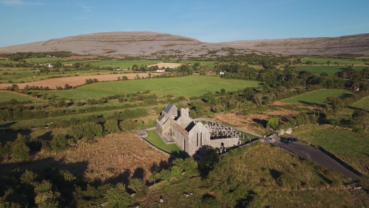 Una ripresa aerea cinematografica delle storiche rovine dell'Abbazia di Corcomroe incastonate nel paesaggio calcareo del Burren, Contea di Clare, Irlanda, durante l'ora d'oro.