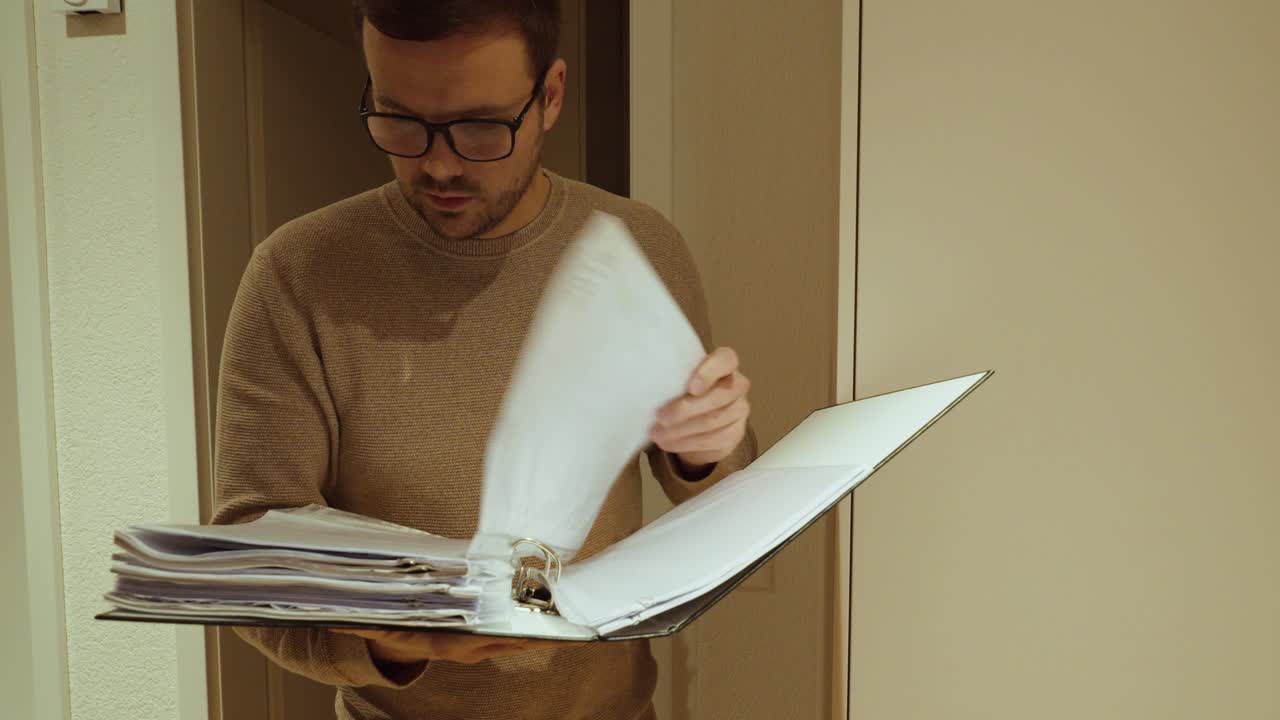 Professionelle stockoptagelser, der viser en mand, som holder og gennemgår en dokumentmappe, hvilket symboliserer revision, compliance-tjek, dokumentgennemgang og kvalitetskontrol inden for erhverv eller administration