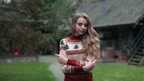 beautiful blonde woman wearing warm sweater standing at the village house. long-haired lady in the countryside background.