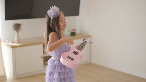 a beautiful little girl is playing the ukulele in the living room for her mom.