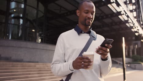 african american businessman walking through city using smart phone