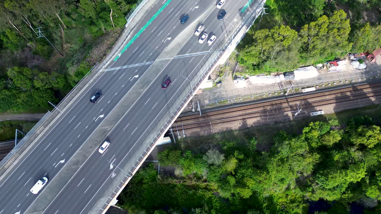 Drone aerial landscape car vehicles transport traffic over train bridge road with railways track with forest in Tuggerah town Central Coast Australia travel urban infrastructure streetlight