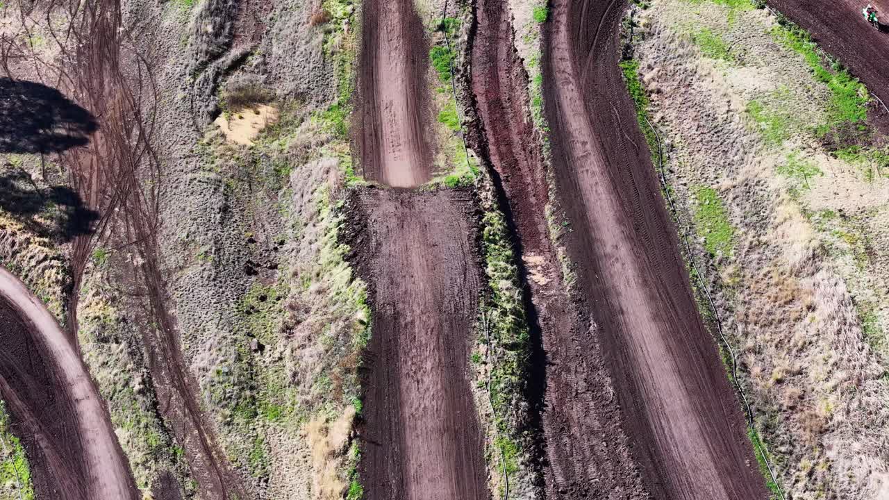 Motorcycle travels on winding dirt trail, aerial view, bright daylight, rural landscape, steady camera