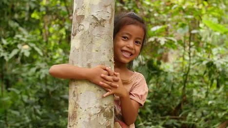 smiling girl hiding behind a tree in a forest