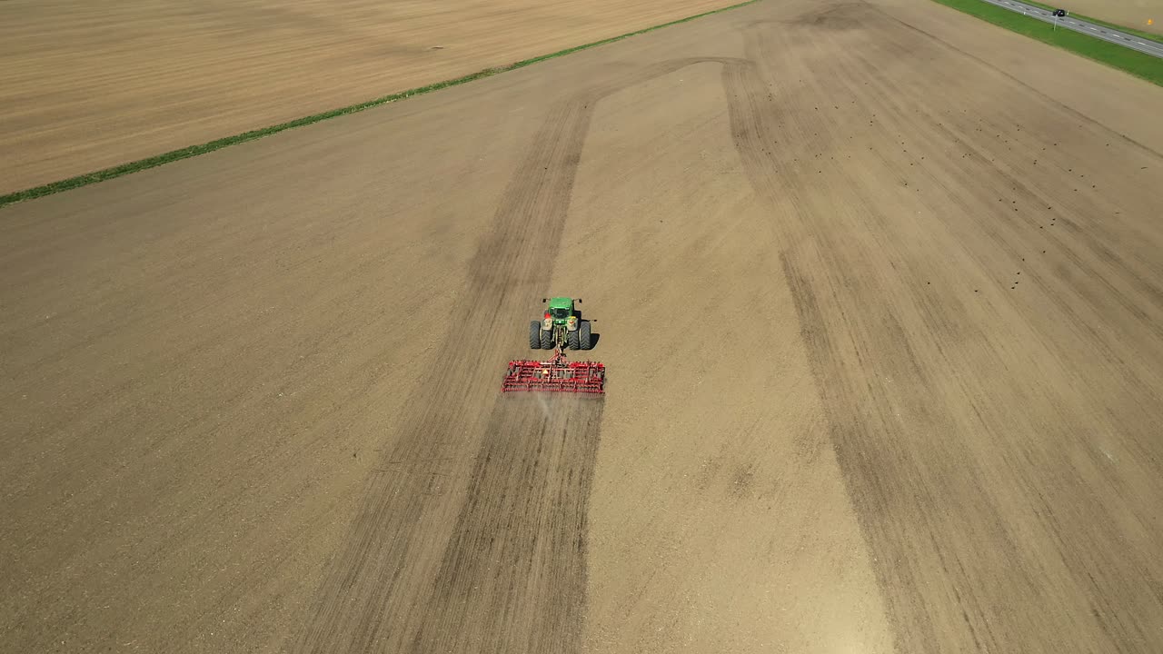 seguimiento de la vista aérea del tractor verde de dos ruedas que cultiva el campo agrícola con el cultivador rojo durante la primavera