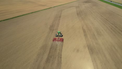 Seguimiento-De-La-Vista-Aérea-Del-Tractor-Verde-De-Dos-Ruedas-Que-Cultiva-El-Campo-Agrícola-Con-El-Cultivador-Rojo-Durante-La-Primavera