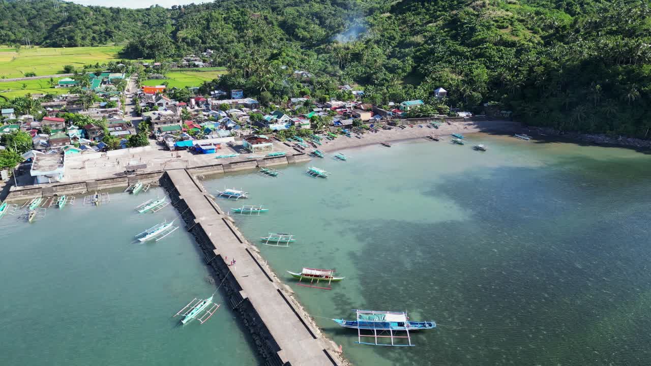 Aerial Flyover Shot of Tropical Island Fishing Village Community and lagoon with traditional Bangka Boats moored at dock, sunny day
