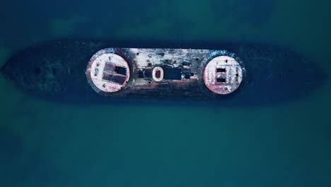 aerial drone shot moving upward, revealing a dramatic shipwreck surrounded by ocean waves, captured from a bird's-eye perspective.