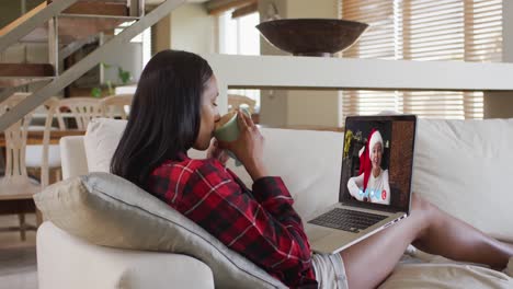 Mixed-race-woman-using-laptop-on-video-chat-with-woman-during-christmas-at-home