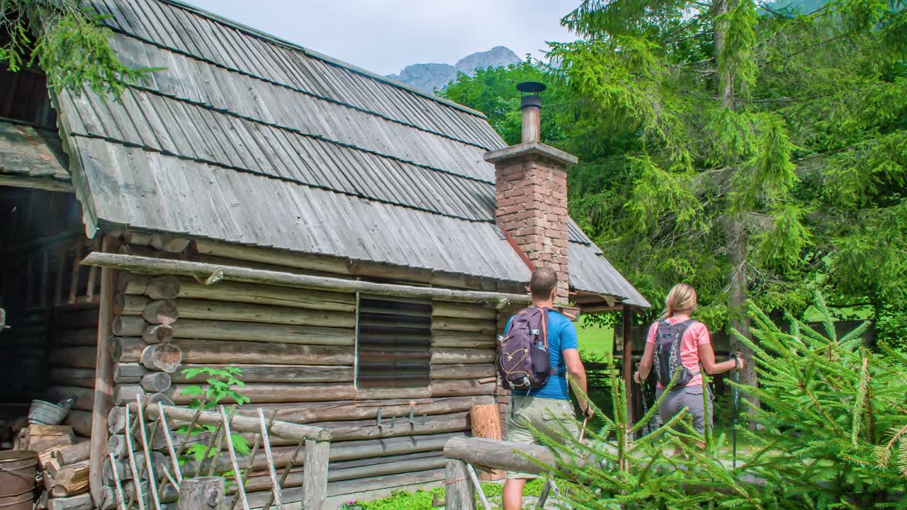 A curious couple of hikers with poles arriving at a wooden cabin in the middle of a green woodland