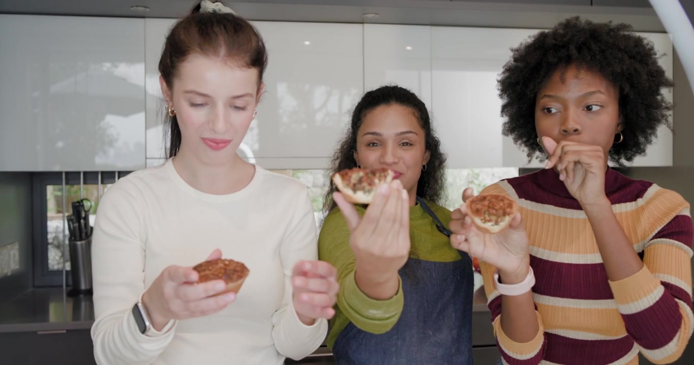 Diverse female friends showing tarts after baking in kitchen rotating and sampling with blue apron