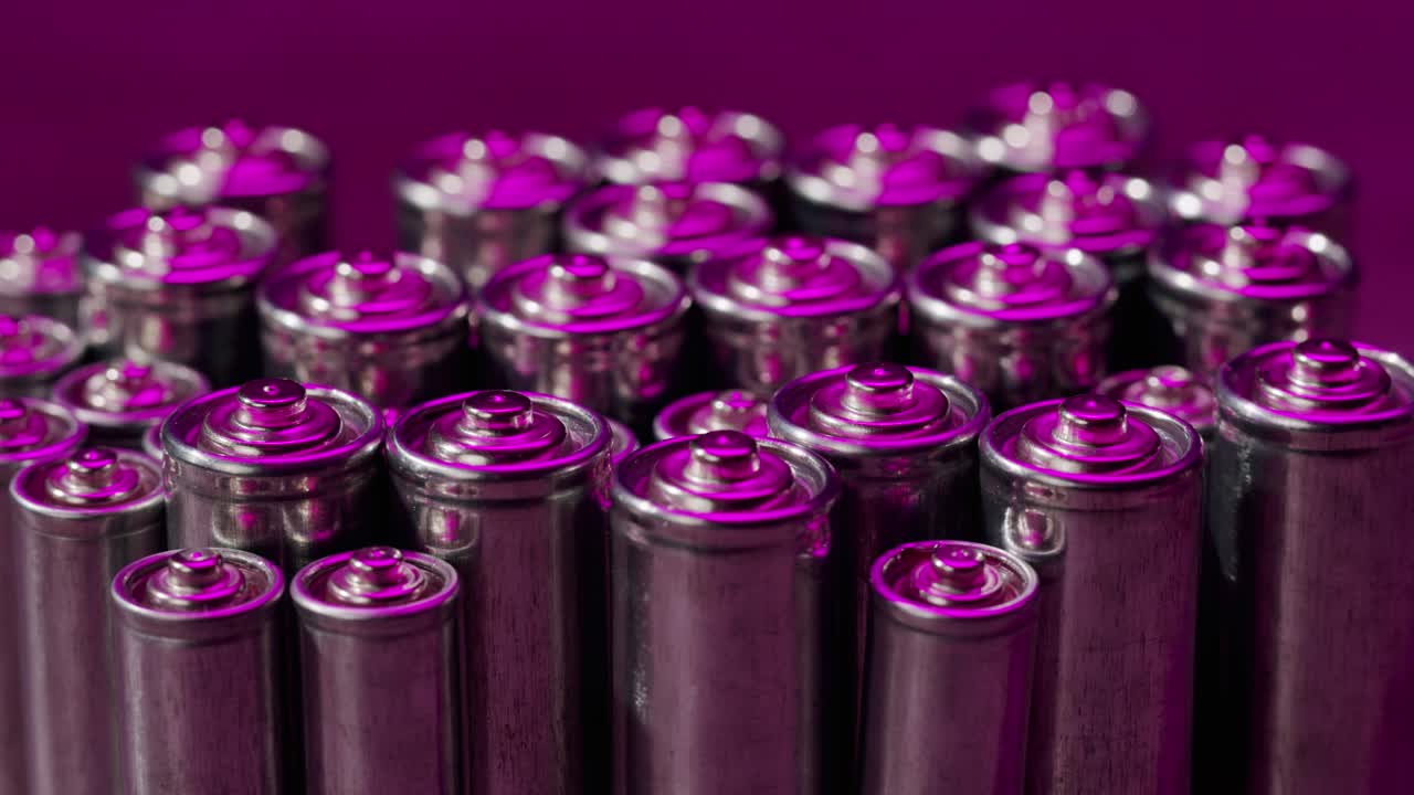 Silver batteries AA and AAA in neon light close-up. Double-A battery is a standard size single cell cylindrical dry battery. Batteries are common in portable electronic devices. An AA battery is composed of a single electrochemical cell that may be either a primary battery or a rechargeable battery.