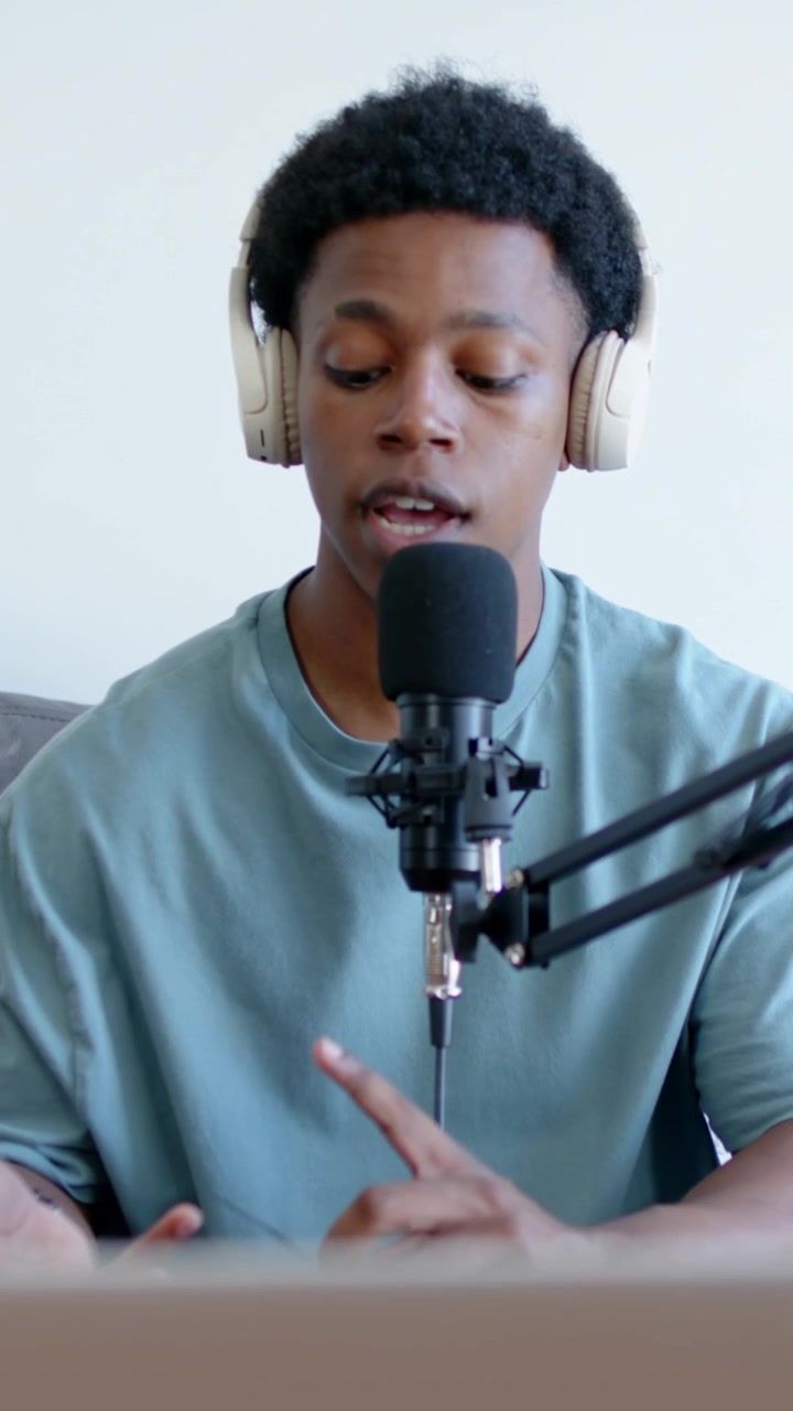 Vertikal video: Øjne åbner, vært taler, kigger på bærbar computer til podcast i hjemmestudie, med mikrofon og hovedtelefoner
