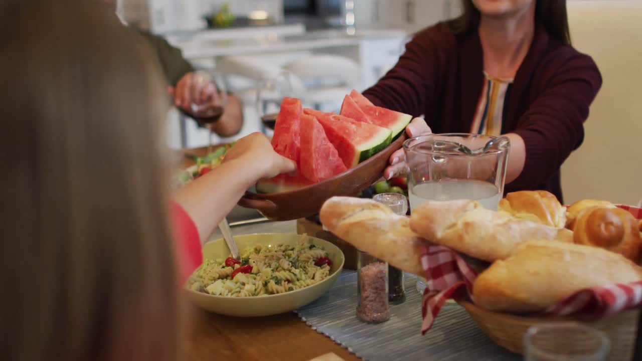 미소 짓는 백인 어머니 가 가족 식사 전 테이블 에서 딸 에게 멜론 조각 을 전달 하고 있다
