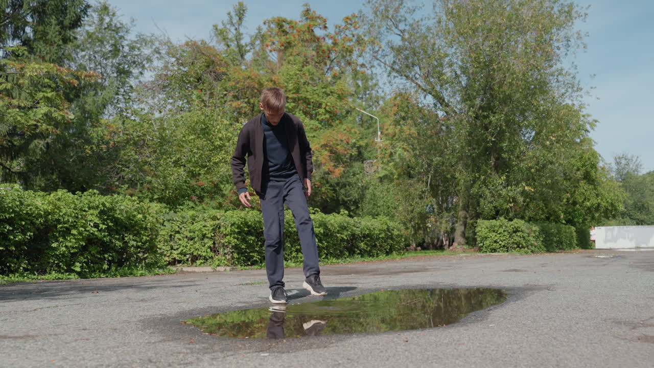 caucasian man kicking puddle in park, casual adult inspects reflection, playful splash, gravel texture, sunny greenery, slow deliberate steps, candid mood, ambient natural light, urban nature