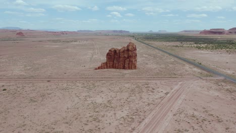 standing butte rock formation in vast arizona desert on navajo reservation, aerial pullback