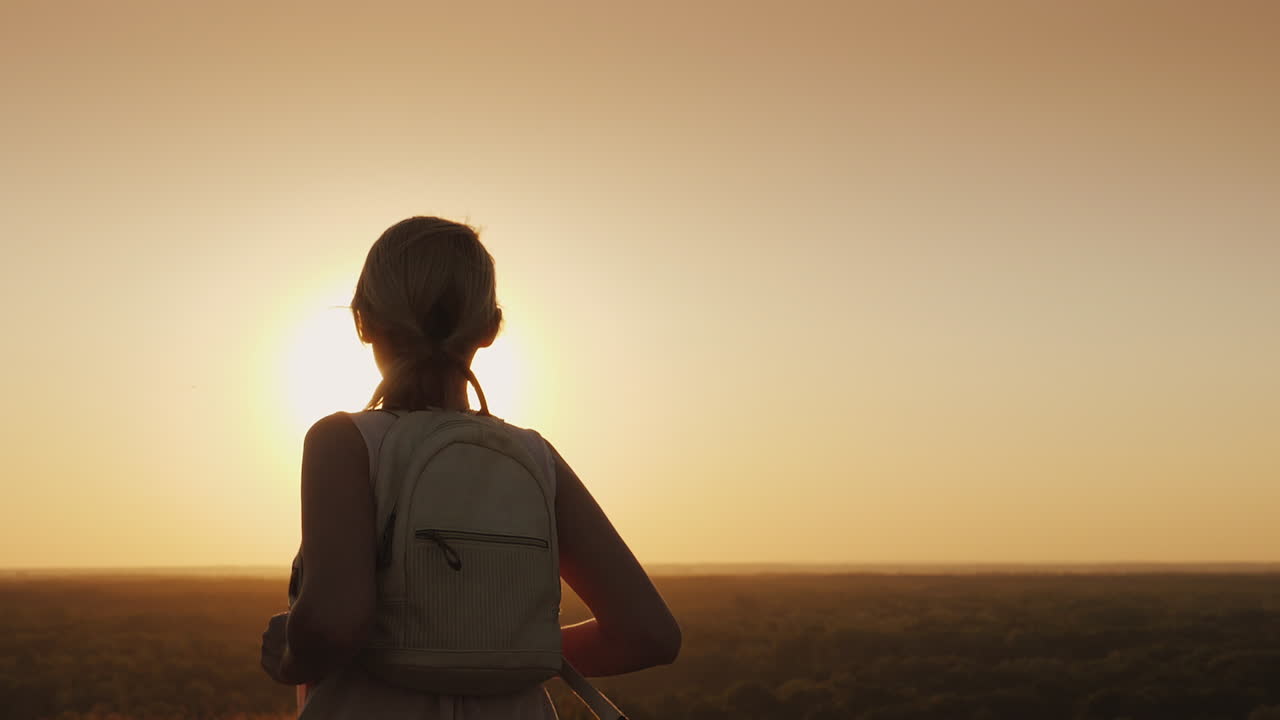 배낭을 메고 있는 한 젊은 여성이 태양을 향해 앞으로 달려갑니다.